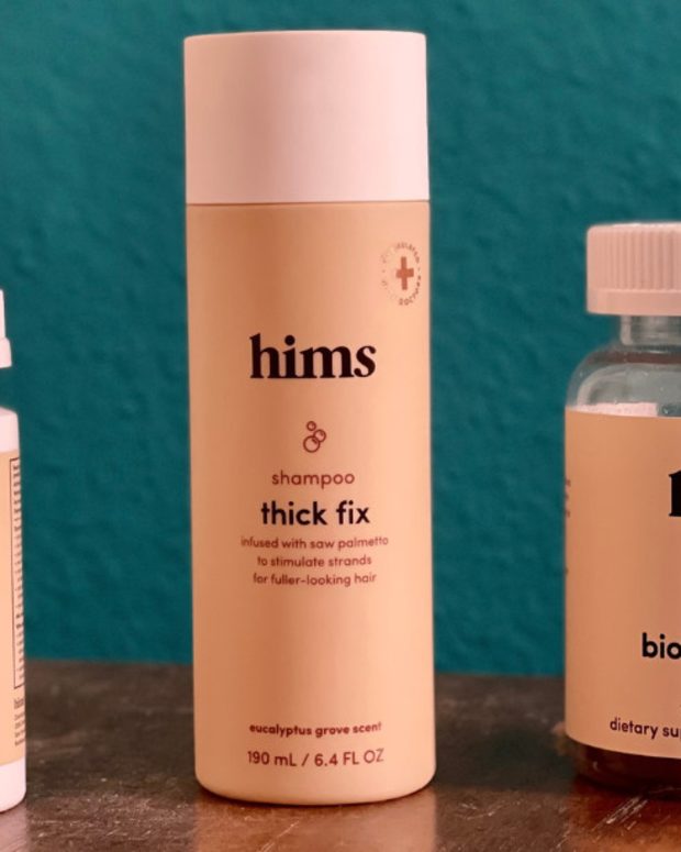 The Hims hair growth serum, shampoo and biotin builder gummies on a wooden table with a blue background.